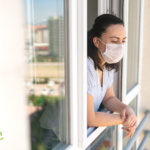 Musty Smells While Quarantining? Might Be Mold | Woman wearing a mask leaning out a window